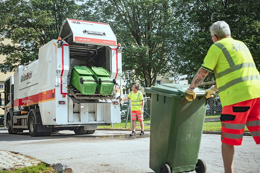 One person pushing a trash can towards a garbage truck